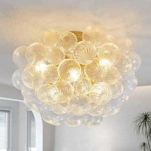 May include: A flush mount ceiling light fixture featuring a cluster of numerous clear, spherical glass globes with a ribbed, swirling texture. The globes are arranged in a dense, rounded formation around a central gold-toned metal base.