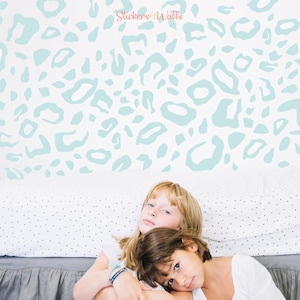 May include: Two children are sitting on a bed with a white and light blue patterned wall behind them. The wall is decorated with a light blue leopard print pattern. The text "Stickers4Walls" is visible in the top center of the image.