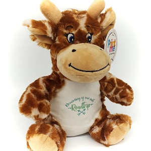 May include: A brown and tan plush giraffe wearing a white shirt with the text "Dreaming of our next Roadtrip" in green lettering. The giraffe has blue eyes and a happy expression.