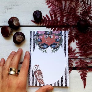 Peut inclure: Un bloc-notes décoratif avec le texte "Petites Notes" et une illustration de hibou. Le bloc-notes présente un motif floral et des rayures noires et blanches. Des châtaignes et du feuillage rouge sont également présents.
