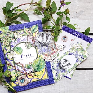 Peut inclure: Ensemble de papeterie illustrée sur le thème de la forêt. Les motifs incluent un blaireau, des éléments floraux et le mot "Forêt". La palette de couleurs comprend des nuances de bleu, de vert et de jaune, sur un fond en bois blanc.