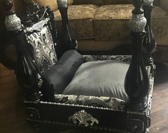 May include: Black and silver dog bed with a four-poster design. The bed has a grey pillow and a black pillow. The bed is decorated with silver accents.