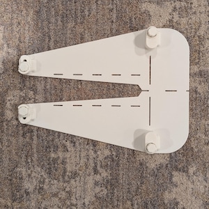Könnte beinhalten: Ein weißer, U-förmiger Möbelhalter mit vier kreisförmigen Befestigungsteilen. Die Halterung hat eine Reihe von gestrichelten Linien und ist für die Montage an einer Wand oder einer anderen Oberfläche vorgesehen. Die Halterung besteht aus einem festen Material.