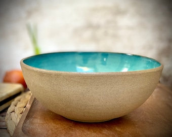 May include: A large, round ceramic bowl with a light brown exterior and a teal blue interior.