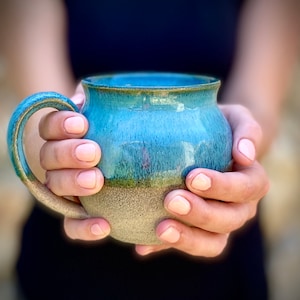 May include: A hand holding a blue and brown ceramic mug with a speckled glaze.
