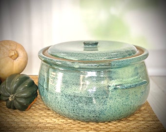May include: A large, green ceramic casserole dish with a lid. The dish has a speckled glaze and two handles on the sides.