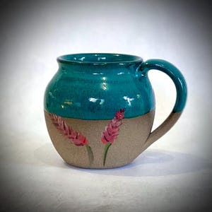 May include: A teal ceramic mug with a brown rim and a handle. The mug is decorated with two pink flowers painted on the side.