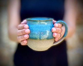 May include: A blue and beige ceramic mug with a speckled glaze. The mug has a rounded body and a handle.