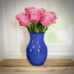May include: A blue ceramic vase with a textured glaze holds a bouquet of pink roses.