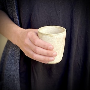 Handgemaakte beker van gebroken wit aardewerk: greeploze keramische koffiekop