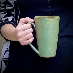 Könnte beinhalten: Eine große, grüne Keramiktasse mit Henkel. Die Tasse hat eine leicht strukturierte Oberfläche und eine dezente Glasur.