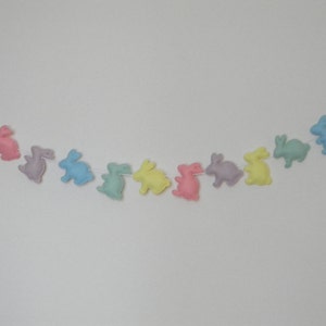 Op de afbeelding: Een pastelkleurige vilt bunny garland met roze, lavendel, lichtblauwe, groene en gele bunnies. De garland is aan een wit touwtje geregen.