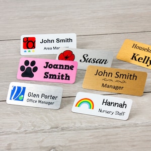 May include: A collection of personalised name tags with various designs and colours. The tags feature names such as "John Smith", "Joanne Smith", "Susan", "Glen Porter", "Hannah", and "Kelly". Some tags include a paw print, a rainbow, a flower, and a logo.