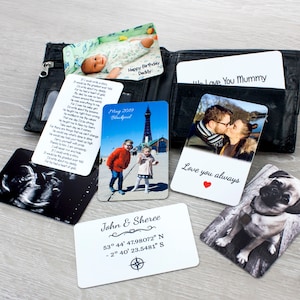 May include: A black leather wallet displaying various personalized photo cards. The cards show images of a baby, a couple, a dog, and a family photo with the text "Happy Birthday Daddy", "Love you always", and "John & Sheree".
