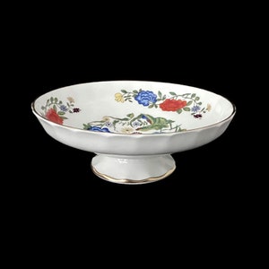 May include: A white ceramic pedestal bowl with a floral design. The bowl has a scalloped edge and a gold trim. The flowers are red, blue, yellow, and green.