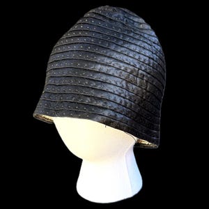 May include: A black cloche hat with horizontal, textured bands and small, evenly spaced dots. The hat is displayed on a white mannequin head against a black background. The brim is slightly turned up.