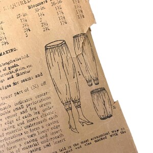 Op de afbeelding: Vintage naaipatroon voor bloomers, met gedetailleerde illustraties van het kledingstuk. Het patroon bevat maten en instructies voor het knippen en in elkaar zetten. Het papier heeft een versleten uiterlijk.