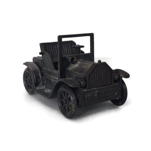 May include: A black vintage car pencil sharpener with a 1917 inscription on the front.