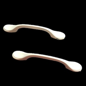 Peut inclure: Deux poignées de meuble en céramique blanche avec une forme arrondie légèrement incurvée.