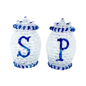 May include: Two clear glass salt and pepper shakers with blue trim and the letters "S" and "P" on the front.
