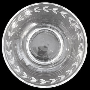 May include: Clear glass bowl with a decorative etched leaf pattern around the rim. The bowl is circular and sits on a black background. The design is simple and elegant.
