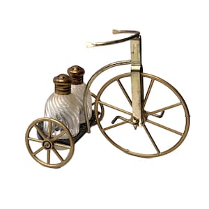 May include: Gold metal salt and pepper shakers shaped like glass bottles on a gold metal tricycle.