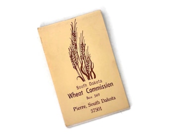 Può includere: Un opuscolo beige con un'illustrazione di una spiga di grano marrone. Il testo recita "South Dakota Wheat Commission Box 549 Pierre, South Dakota 57501".