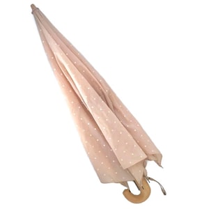 Peut inclure: Un parapluie rose avec des pois blancs et une poignée en bois.