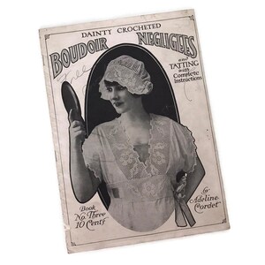 Può includere: Una copertina di libro vintage con una donna che indossa una vestaglia e un cappello di pizzo bianco, tenendo uno specchio da mano. Il testo della copertina recita "Dainty Crocheted Boudoir Negligees and Tatting with Complete Instructions" e "Book No. Three 10 Cents" di Adeline Cordet.