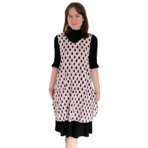 Könnte beinhalten: Ein ärmelloses Kleid mit einem geometrischen Muster in Weiß-, Marineblau- und Orangetönen. Das Kleid hat einen V-Ausschnitt und eine lockere Passform.