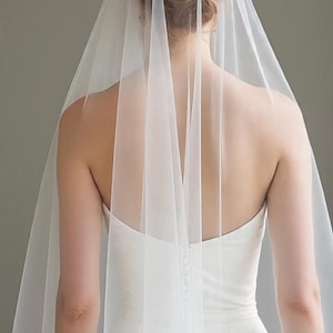 May include: A sheer, floor-length white bridal veil made of fine tulle fabric. The veil is attached to the hair and drapes down the back, extending past the shoulders and torso, creating a soft, layered effect over a strapless white gown.