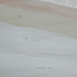 May include: Four layers of English Netting fabric in distinct shades, labeled as Blush, Ivory, White, and Diamond Off White. The sheer, fine-mesh material is draped in soft, horizontal folds, showcasing the subtle color variations of each textile layer.