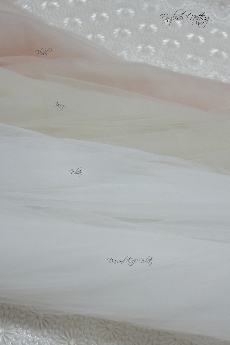 May include: Four layers of English Netting fabric in distinct shades, labeled as Blush, Ivory, White, and Diamond Off White. The sheer, fine-mesh material is draped in soft, horizontal folds, showcasing the subtle color variations of each textile layer.