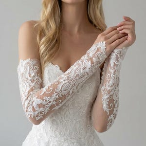 May include: White lace bridal sleeves with intricate floral patterns. The sleeves are long and fitted, with a sheer fabric base. The dress features a sweetheart neckline and a tulle skirt, creating an elegant bridal look.