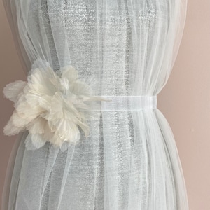 Op de afbeelding: Een witte tule jurk met een witte bloemenversiering op de taille.