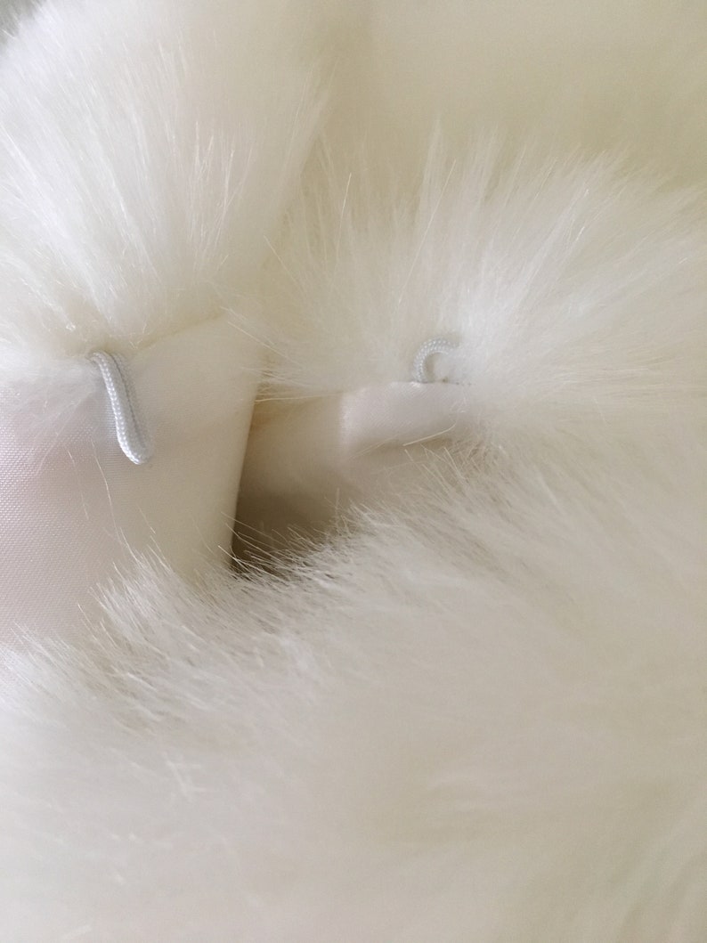 May include: Close-up of a white faux fur fabric with two white loops sewn into the fabric.