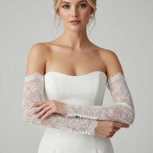 May include: A strapless white wedding dress with delicate lace sleeves. The sleeves are long, fitted, and adorned with intricate floral lace patterns. The dress has a simple, elegant design, perfect for a bride.