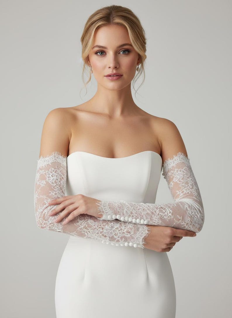 May include: A strapless white wedding dress with delicate lace sleeves. The sleeves are long, fitted, and adorned with intricate floral lace patterns. The dress has a simple, elegant design, perfect for a bride.