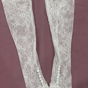 May include: Two white lace sleeves with floral patterns and scalloped edges. Each sleeve has a row of small, round buttons. The sleeves are made of delicate, sheer lace.