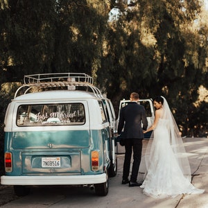 May include: A blue and white vintage van with a "Just Married!" sign on the back window. A bride and groom are getting into the van.