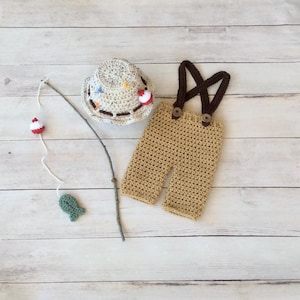 May include: Crocheted fishing-themed baby outfit with a hat, overalls, and a fishing rod with a fish and bobber.