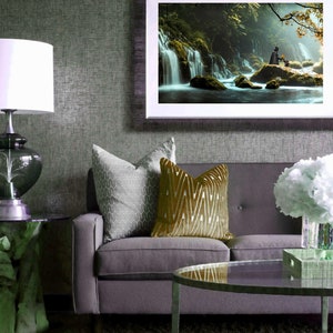 May include: A gray sofa with two throw pillows, one with a geometric pattern and the other with a gold chevron pattern. A framed picture of a waterfall in a forest hangs on the wall above the sofa. A glass coffee table sits in front of the sofa.