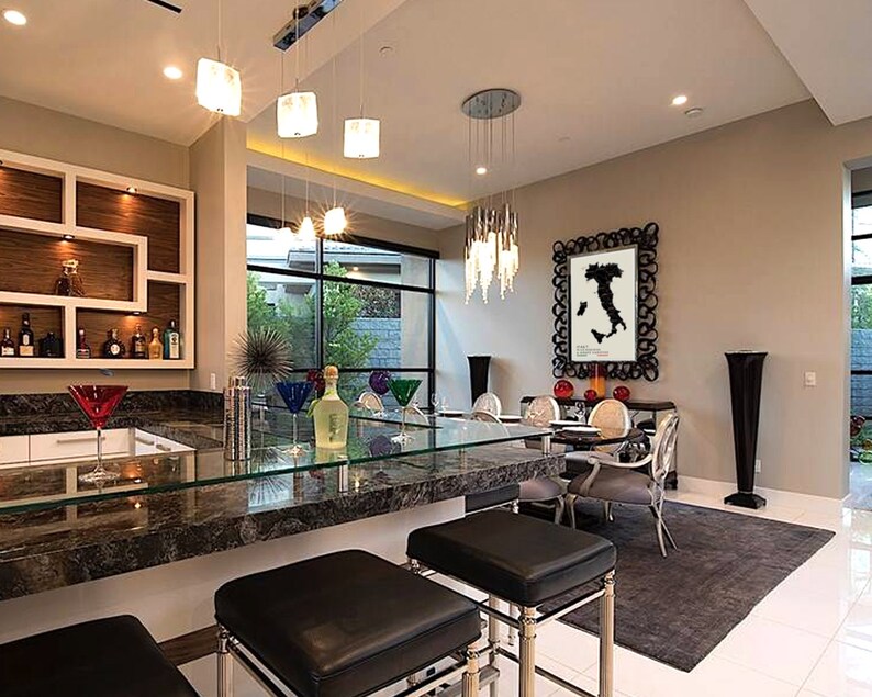 May include: A modern kitchen with a bar area featuring a granite countertop and black leather bar stools. The bar area has a glass top and a built-in liquor cabinet. The kitchen also has a dining area with a glass table and chairs. The dining area has a large black and white framed print of a map of Italy on the wall.