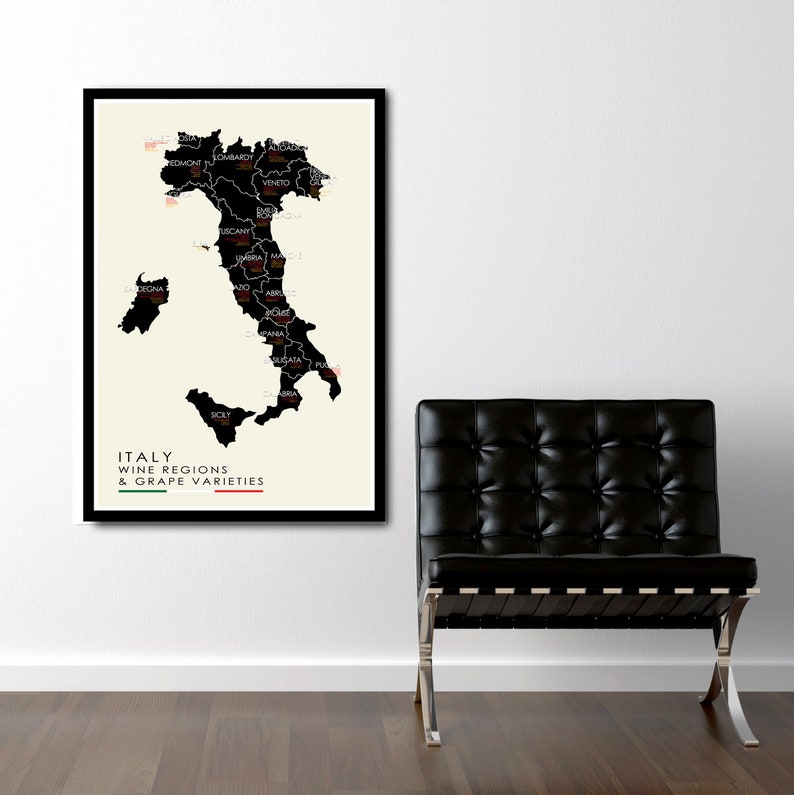 May include: A black and white map of Italy with the wine regions and grape varieties labeled. The map is framed in black and hanging on a white wall. A black leather chair with a chrome frame is in the foreground.