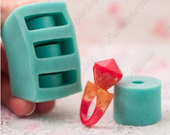 May include: Two silicone molds: one clear with three vertical compartments holding blue flowers, and another teal mold with three circular cavities. A red and orange resin ring and a teal cylinder are also shown.