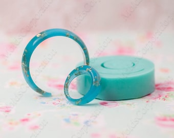 May include: A turquoise resin bangle and ring, both with gold leaf inclusions. A round, light blue silicone mould is also present. The jewellery is set against a floral backdrop.