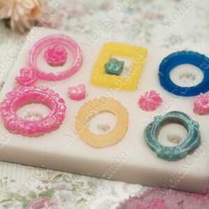 Puede incluir: Un molde de silicona blanco con varias formas, incluyendo marcos y detalles florales, en rosa, amarillo y azul. El molde presenta diseños detallados para la creación de elementos decorativos.