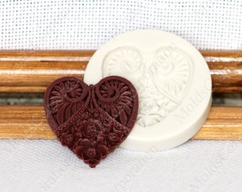 May include: A dark red heart-shaped mould with detailed floral and swirl designs, alongside a white silicone mould. The design features roses and other floral elements, ideal for crafting projects.