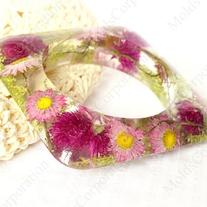 Peut inclure: Bracelet jonc carré en résine transparente avec des fleurs roses et jaunes et du feuillage vert. Ce bijou unique présente un thème botanique. Les fleurs sont conservées dans la résine transparente.
