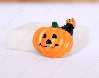 May include: A small, orange Halloween pumpkin figurine with a smiling face, black eyes, and a black mouth. A small black cat is perched on top of the pumpkin. The pumpkin has a green stem.